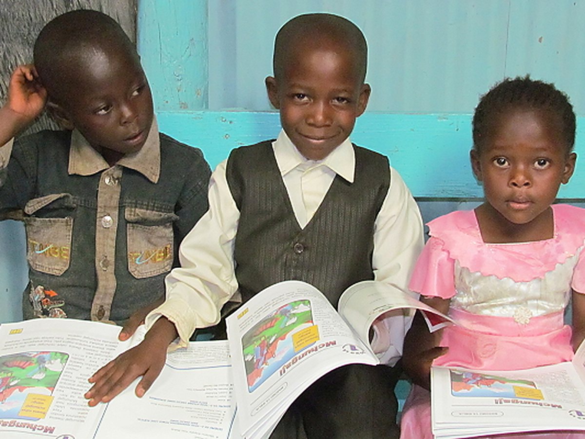 Three children holding open Character Code for Life Bible study books in their own language.